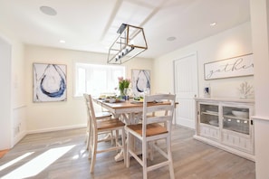 A dining area with a wooden table, white chairs, a chandelier, and artwork on the walls.