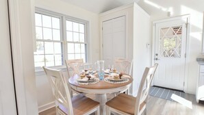 Un comedor con una mesa redonda, sillas blancas y una puerta con un panel de vidrio decorativo.