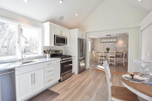 A modern kitchen with white cabinets, stainless steel appliances, and a dining area with a wooden table and chairs.