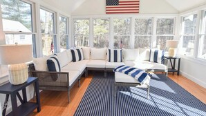 Una habitación iluminada por el sol con un amplio ventanal, un sofá modular, un tapete a rayas y una bandera estadounidense.