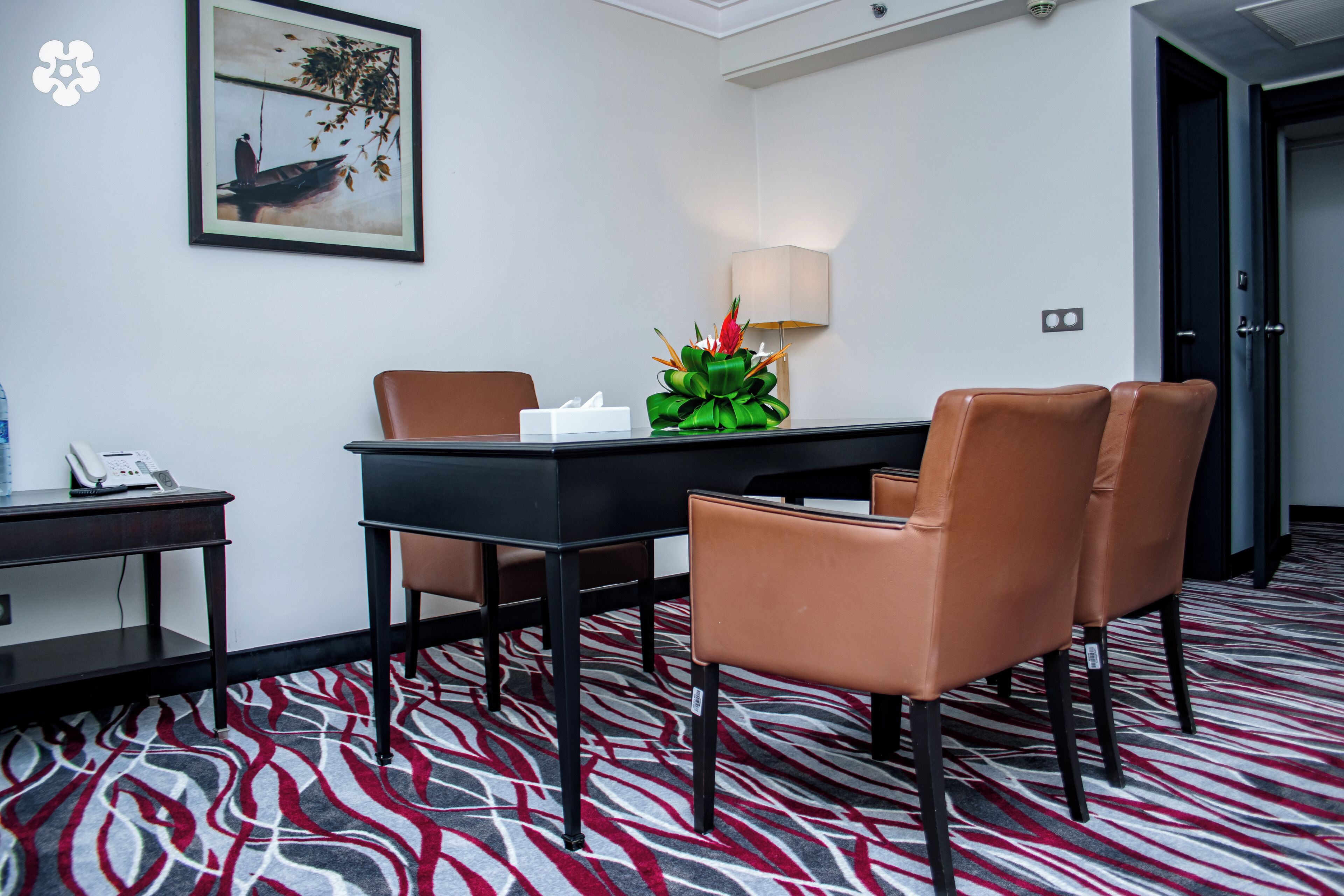 Une chambre d’hôtel équipée d’une table à manger, de quatre chaises, d’une lampe, d’un téléphone et d’un tableau encadré au mur.