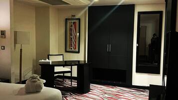 A hotel room with a bed, a desk, a chair, a wardrobe, and a large mirror.