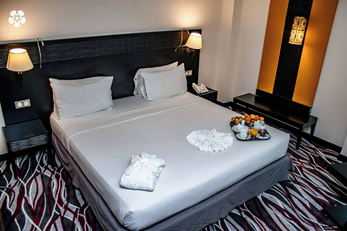 A neatly made bed with white linens, a bedside table with a lamp, and a tray with towels and toiletries.