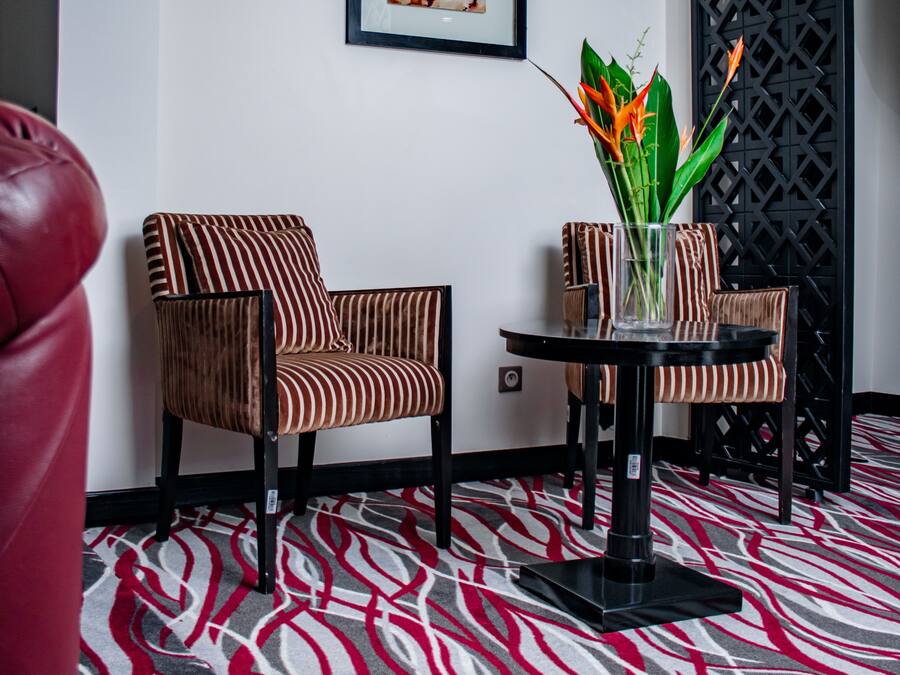 Una habitación con sillas a rayas, una pequeña mesa con un florero y una alfombra estampada.
