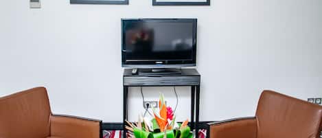 A room with a black TV on a stand, two brown leather chairs, a table with a black top, and two framed artworks on the wall.