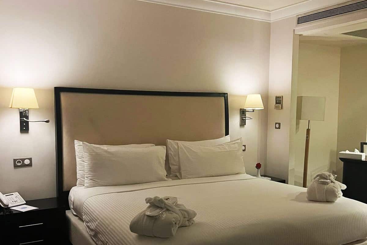 A hotel room with a large bed, two bedside lamps, a telephone, and a small table with a lamp.