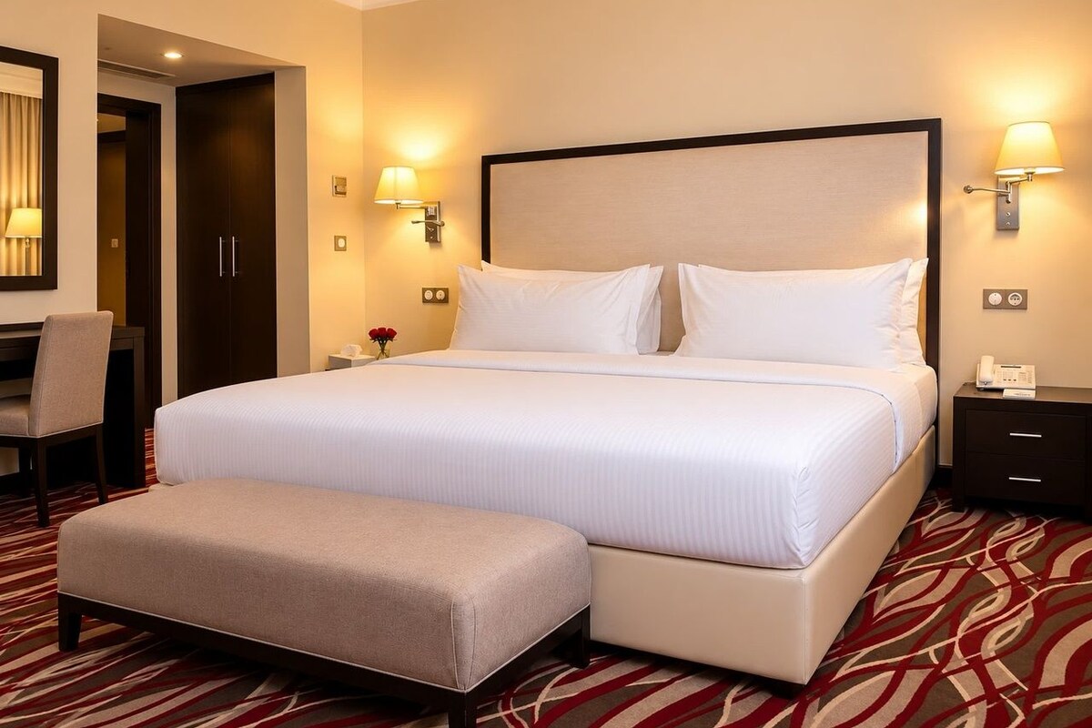 Una habitación de hotel con una cama grande, un reposapiés, un escritorio y dos lámparas de noche.