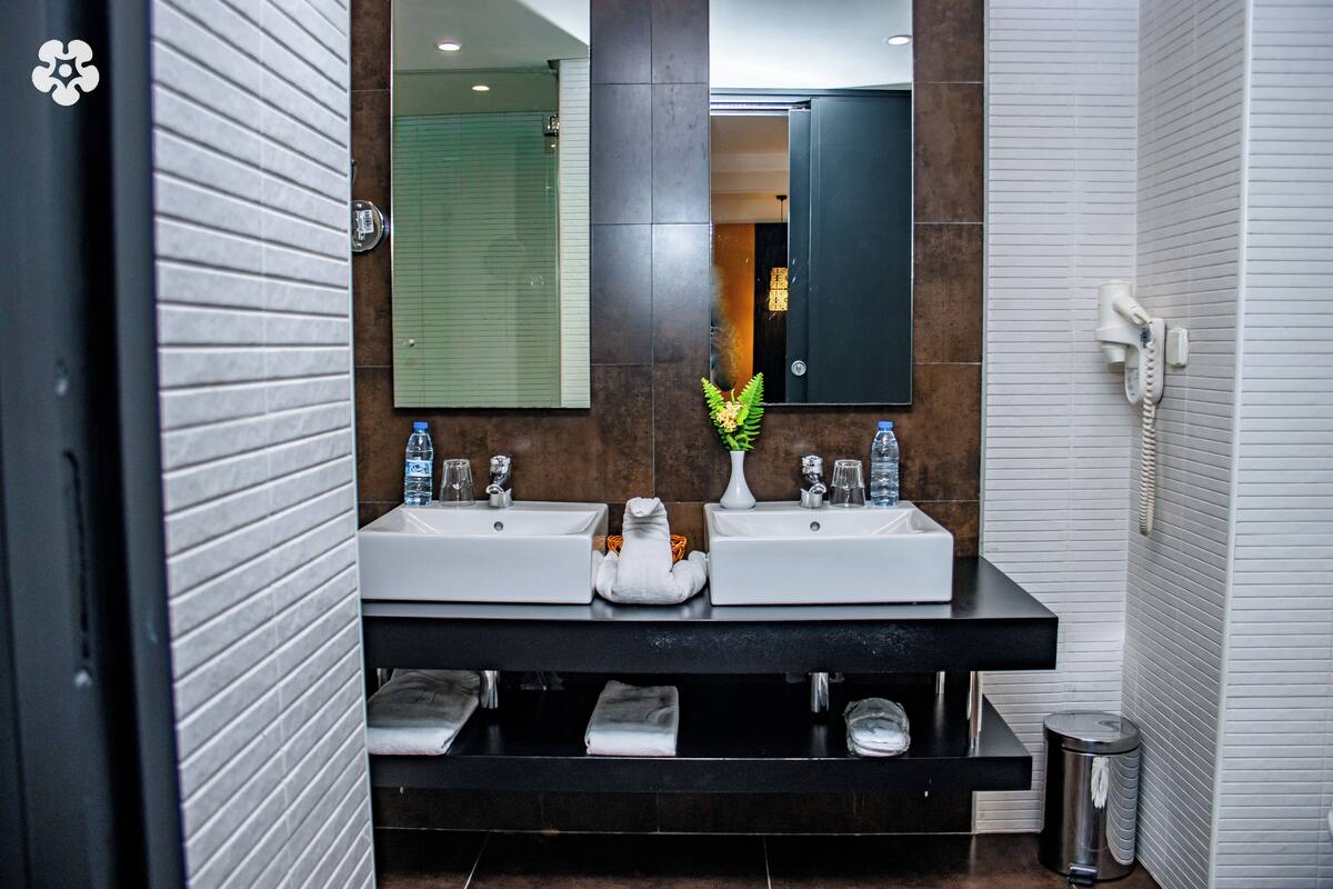 A modern bathroom with two sinks, a mirror, and a trash bin.