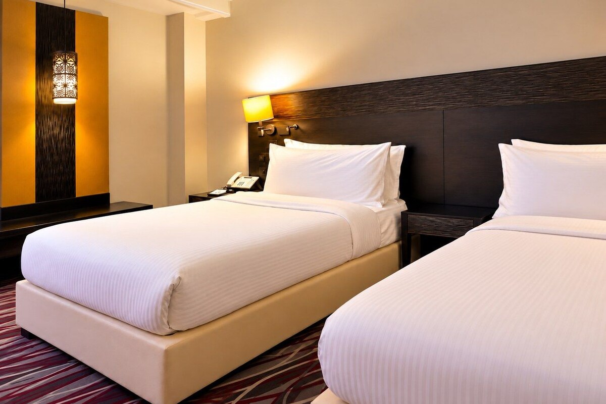 Una habitación de hotel con dos camas, una mesita de noche con lámpara y una lámpara de pared.