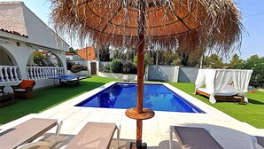 Una piscina con sillones de descanso, una pérgola y un edificio blanco al fondo.