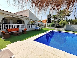 Una piscina con un borde de baldosas, mobiliario exterior y una zona de estar cubierta.