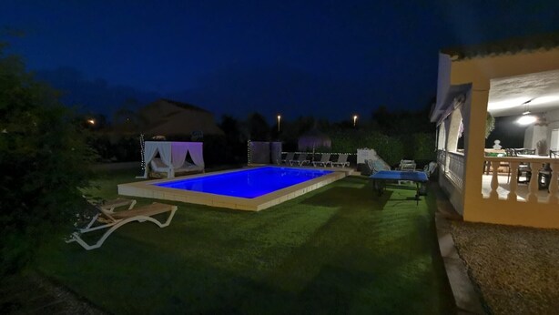 Piscina ao ar livre com um pequeno deck, cercada por um gramado bem cuidado e algumas cadeiras de sol.
