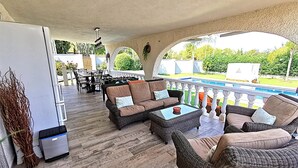 Um pátio externo com mobiliário de vime, piscina e vista para o jardim.
