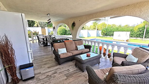 Un patio al aire libre con mobiliario de mimbre, piscina y vistas al jardín.