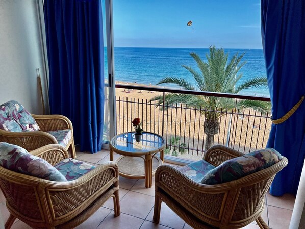 A balcony with wicker furniture, a glass table, and a view of the beach and ocean.