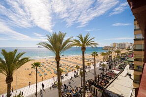 A beach with palm trees, a promenade, and buildings in the background.