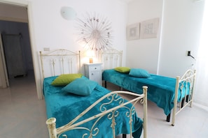 Une chambre avec deux lits, une table de chevet, un élément décoratif mural et une porte donnant sur une autre pièce.