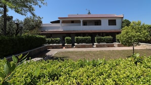 Un bâtiment à deux étages, doté d’un toit plat, entouré de verdure et surplombé d’un ciel dégagé.