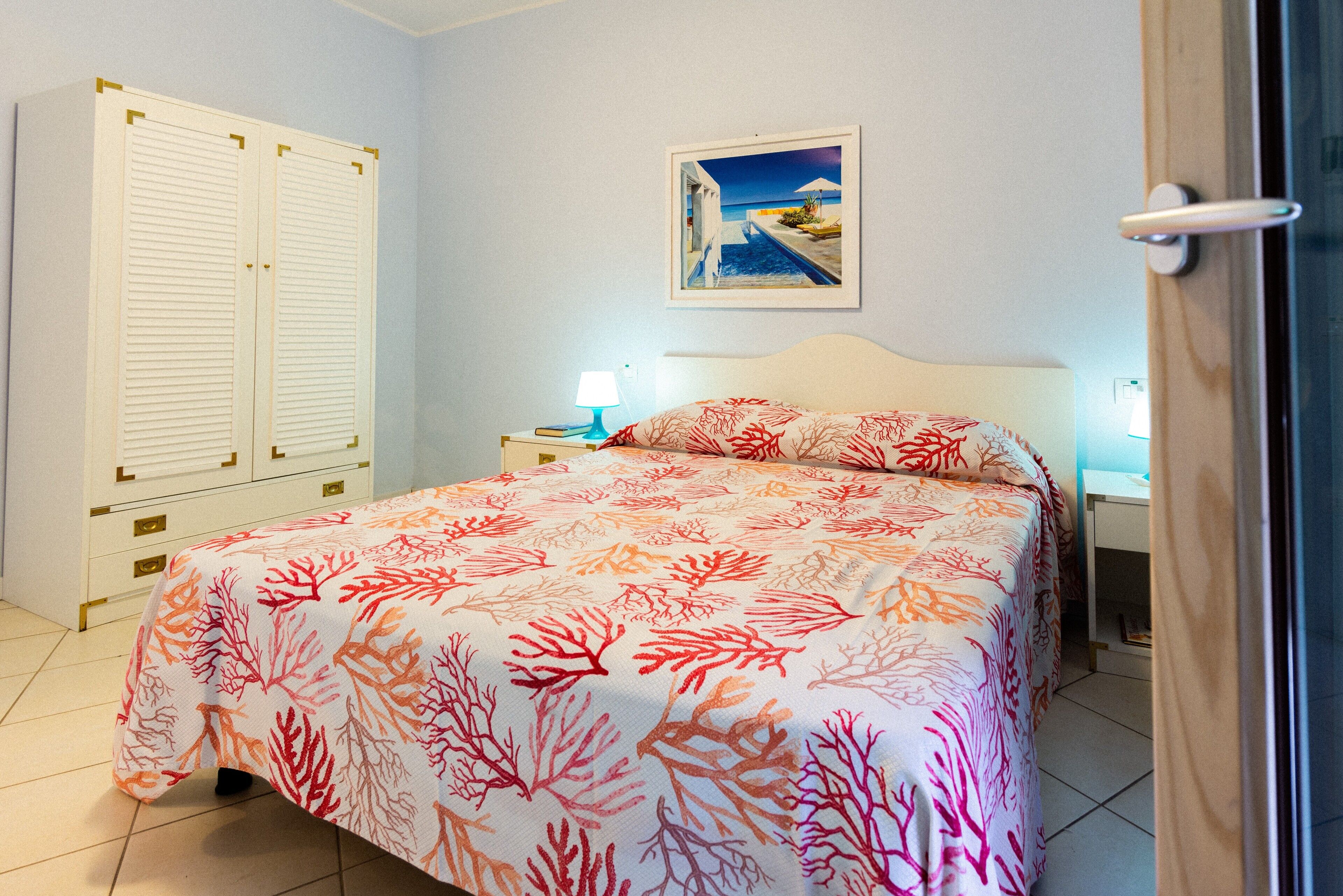 A bedroom with a bed, a nightstand, a lamp, a wardrobe, and a painting on the wall.
