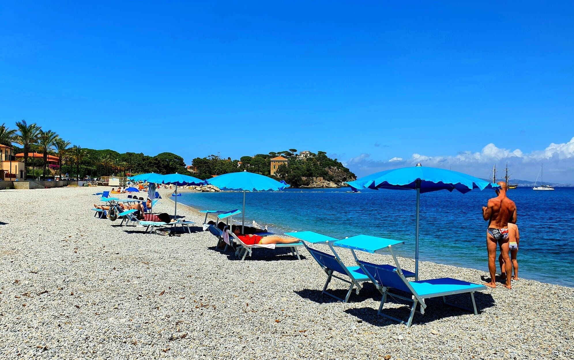 A beach with rows of sun loungers and umbrellas, a clear blue sky, and a calm sea.