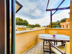 Un balcon avec une table et des chaises, une vue sur les bâtiments environnants et un ciel dégagé.