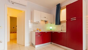 Una cocina moderna con armarios blancos y rojos, un salpicadero de azulejos y un baño visible en el pasillo contiguo.