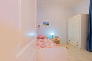 Une chambre à coucher comprenant un lit, une table de chevet, une lampe, une armoire et un petit tableau décoratif mural.