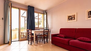 Una habitación con un sofá rojo, una mesa de comedor con sillas y un ventanal corredero que da a un espacio exterior.