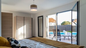 A bedroom with a large bed, a sliding glass door to a balcony with a pool, and a ceiling light. - Private pool villa - 5* (Plurien)