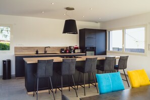 Una cocina moderna con una isla central, taburetes de bar y un ventanal grande.