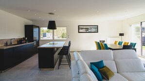A modern kitchen with a central island, a dining area with a table and chairs, and a living area with a sofa and cushions. - Private pool villa - 5* (Plurien)