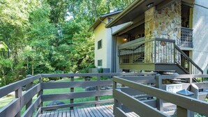 Une terrasse en bois, avec un bâtiment en pierre en arrière-plan, le tout entouré de verdure.