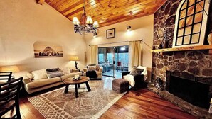 Un salon chaleureux avec une cheminée en pierre, un plafond en bois et une grande fenêtre.