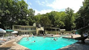 Un espace piscine doté de chaises longues et de parasols, entouré d’arbres.