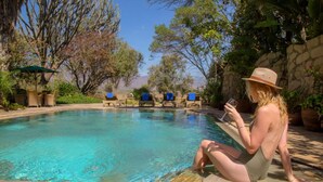 A poolside area with lounge chairs and a person sitting by the pool. - Chui Lodge (Naivasha)