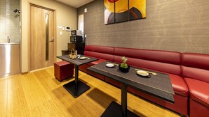 Un área de comedor moderna con un sofá rojo, dos mesas negras y un cuadro abstracto colgado en la pared.