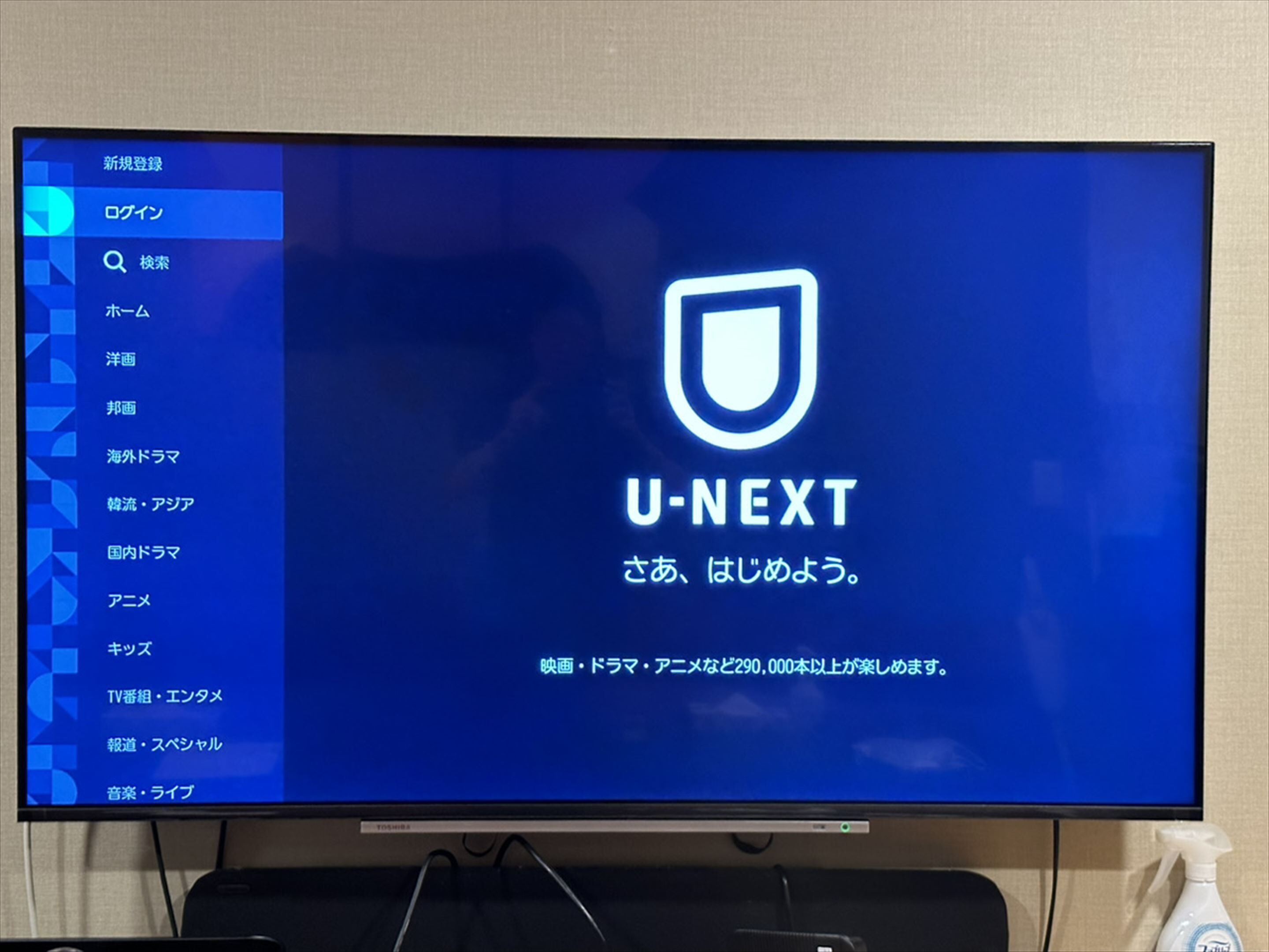 A television screen displaying the U-NEXT logo and Japanese text, with a list of menu options on the left.