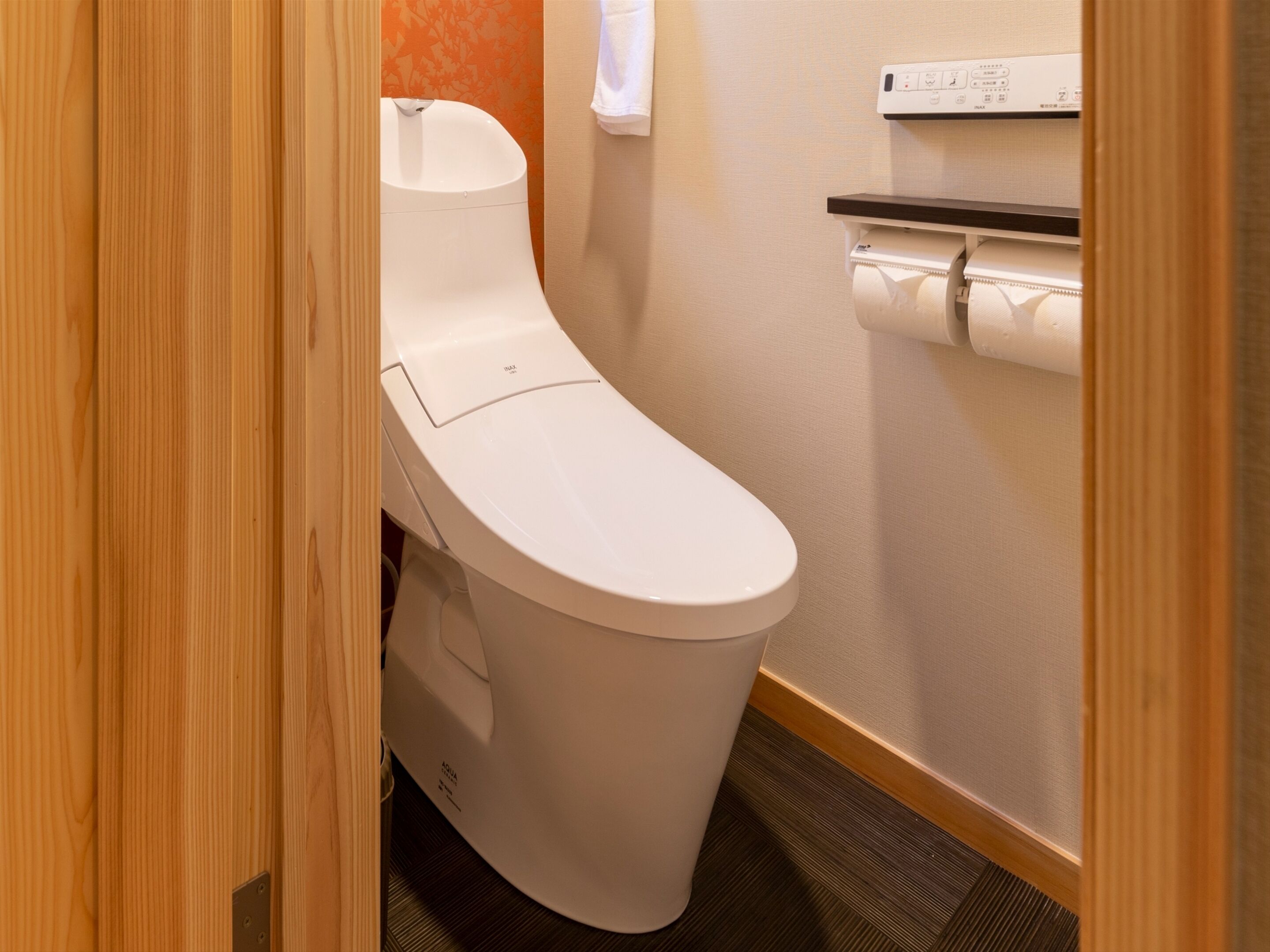 A white toilet with a tank, a toilet paper holder on the wall, and a wooden floor.