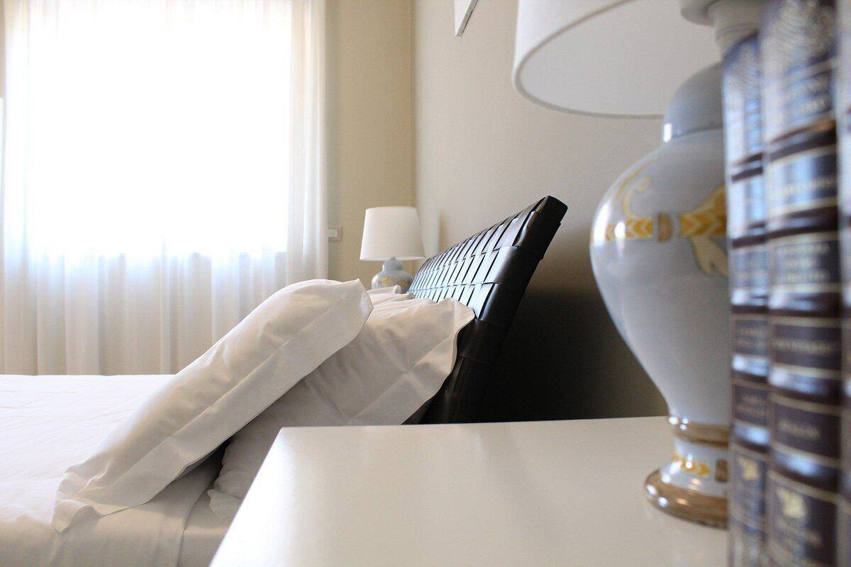 A hotel room with a bed, white bedding, a lamp, and a vase.
