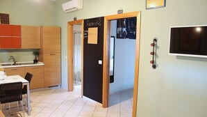 Una cocina con una mesa de comedor, sillas y una pequeña isla. Se ve una puerta con la etiqueta 'Room n2' que da a otra habitación.