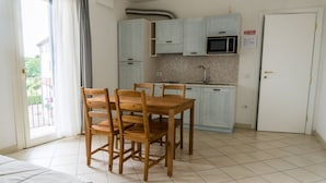Ett kompakt kök med ljusblå skåp, en mikrovågsugn och ett handfat. I förgrunden står ett matbord med stolar.