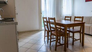 Un coin repas avec une table et des chaises en bois, un coin cuisine avec un évier, et une vue à travers une porte avec des rideaux.