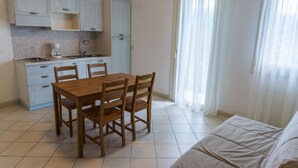 Une cuisine compacte avec des meubles blancs, une table à manger avec des chaises et une grande fenêtre ornée de rideaux légers.