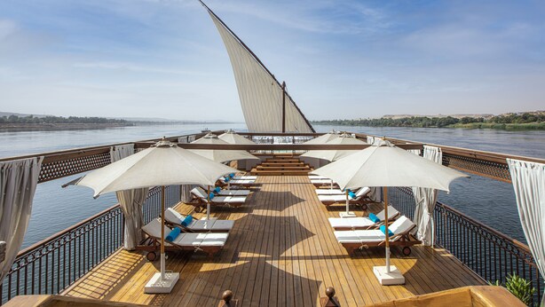Une terrasse dotée de chaises longues et de parasols, avec vue sur une rivière.