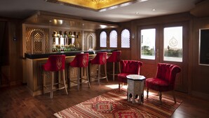 Un coin bar avec des tabourets de bar en bois et un fauteuil à revêtement rouge, un tapis à motifs et un luminaire décoratif au plafond.