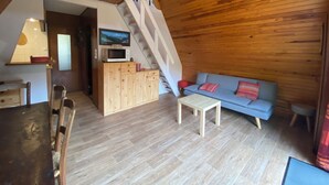 Interior acogedor de una cabaña con una escalera de madera, un sofá azul, una mesa de comedor de madera y una zona de cocina con microondas.