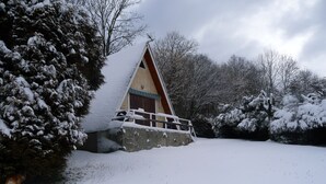 Una cabaña nevada con un porche de madera y un muro de piedra.