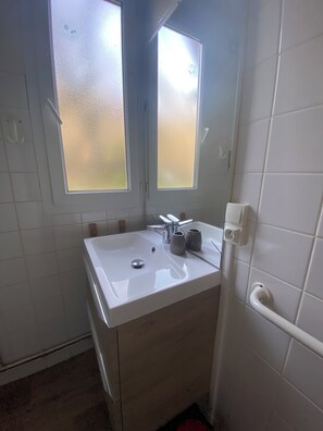 A bathroom with a white sink, two frosted windows, a mirror, and a towel rack.