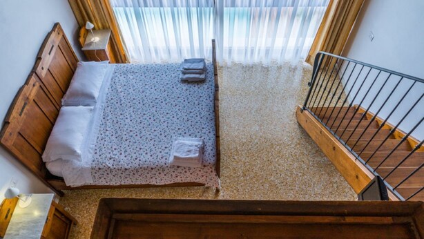 Une chambre à coucher avec un lit en bois, une petite table de chevet et une fenêtre ornée de rideaux légers.