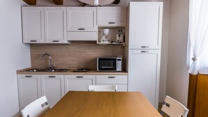 Une cuisine compacte avec des meubles blancs, un four à micro-ondes et un évier. On y trouve une table en bois et deux chaises blanches.